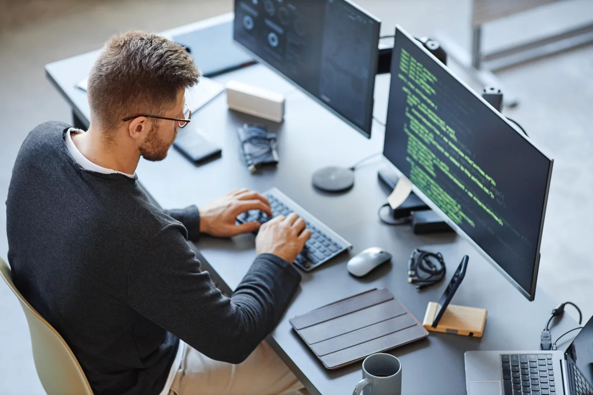 Male IT tester types on keyboard in front of two monitors